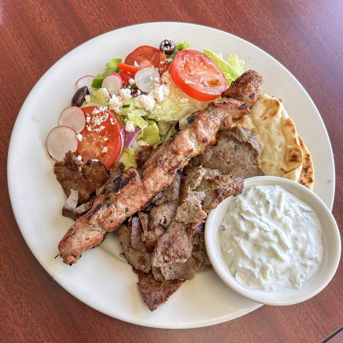 A combo platter with gyro meat, a grilled souvlaki skewer, pita, Greek salad and a side of tzatziki.