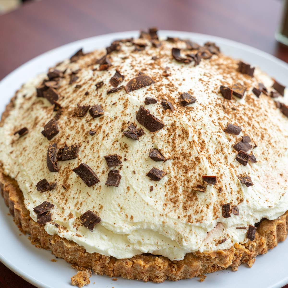 A whole homemade cream pie topped with whipped cream, chocolate shavings and dusted cinnamon.
