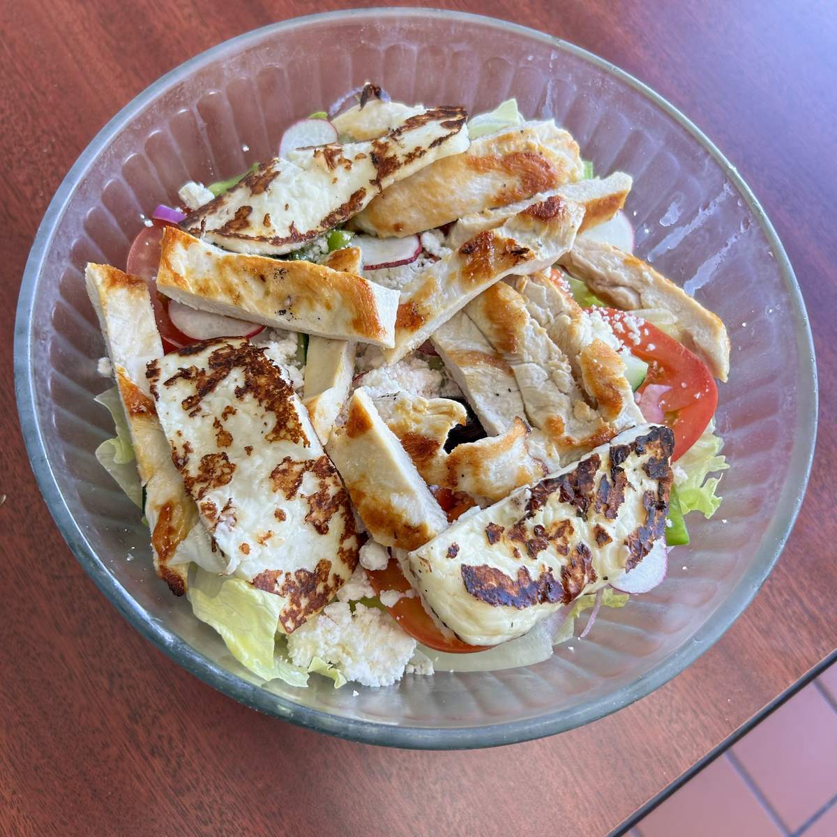 Grilled halloumi salad with sliced grilled chicken, feta, tomato and radish in a glass bowl.