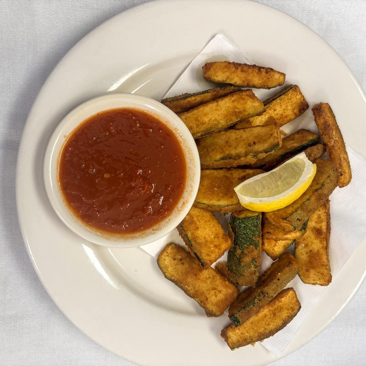 Golden fried zucchini served with a lemon wedge and a side of marinara sauce.