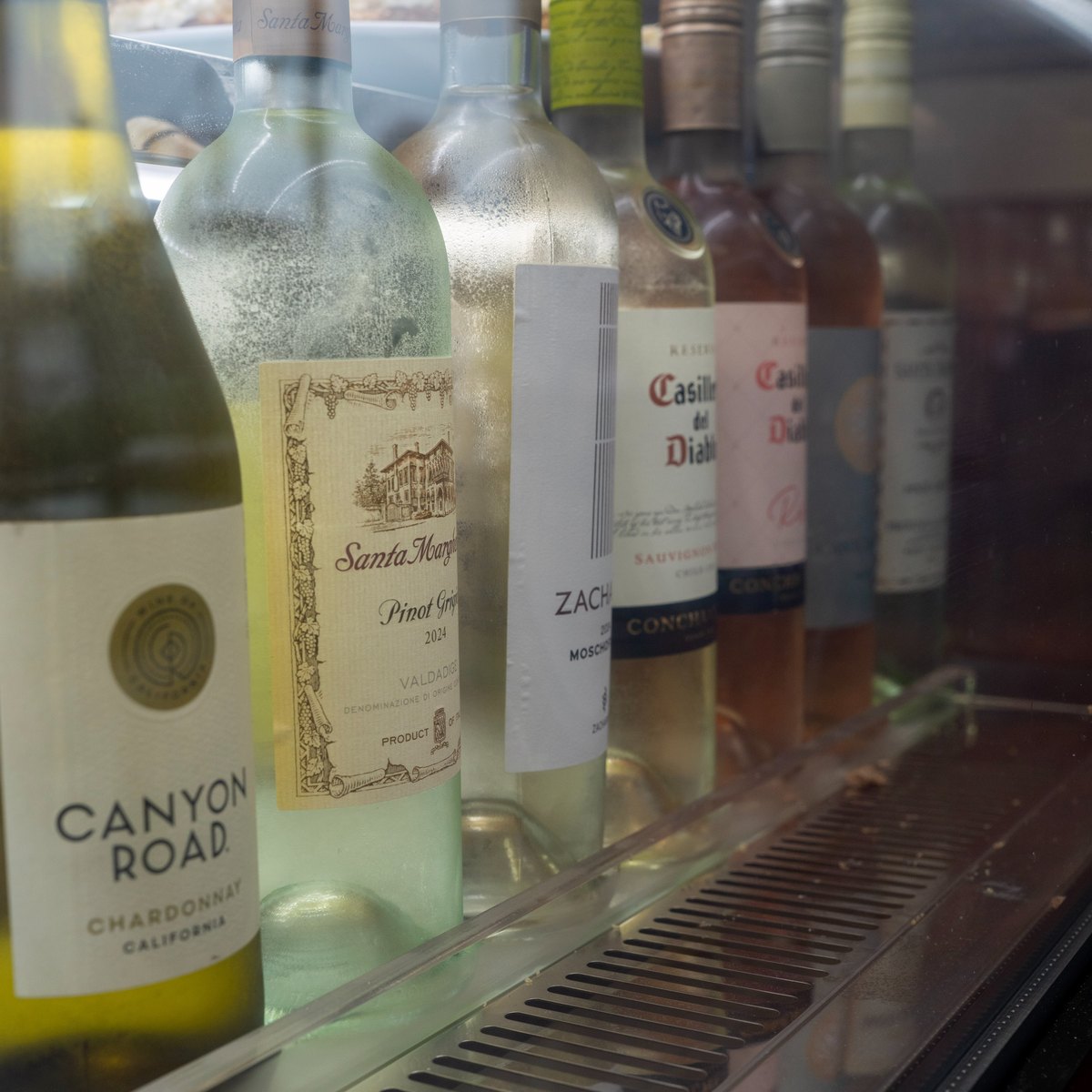 A row of white and rose wine bottles chilling in the restaurant's display refrigerator.