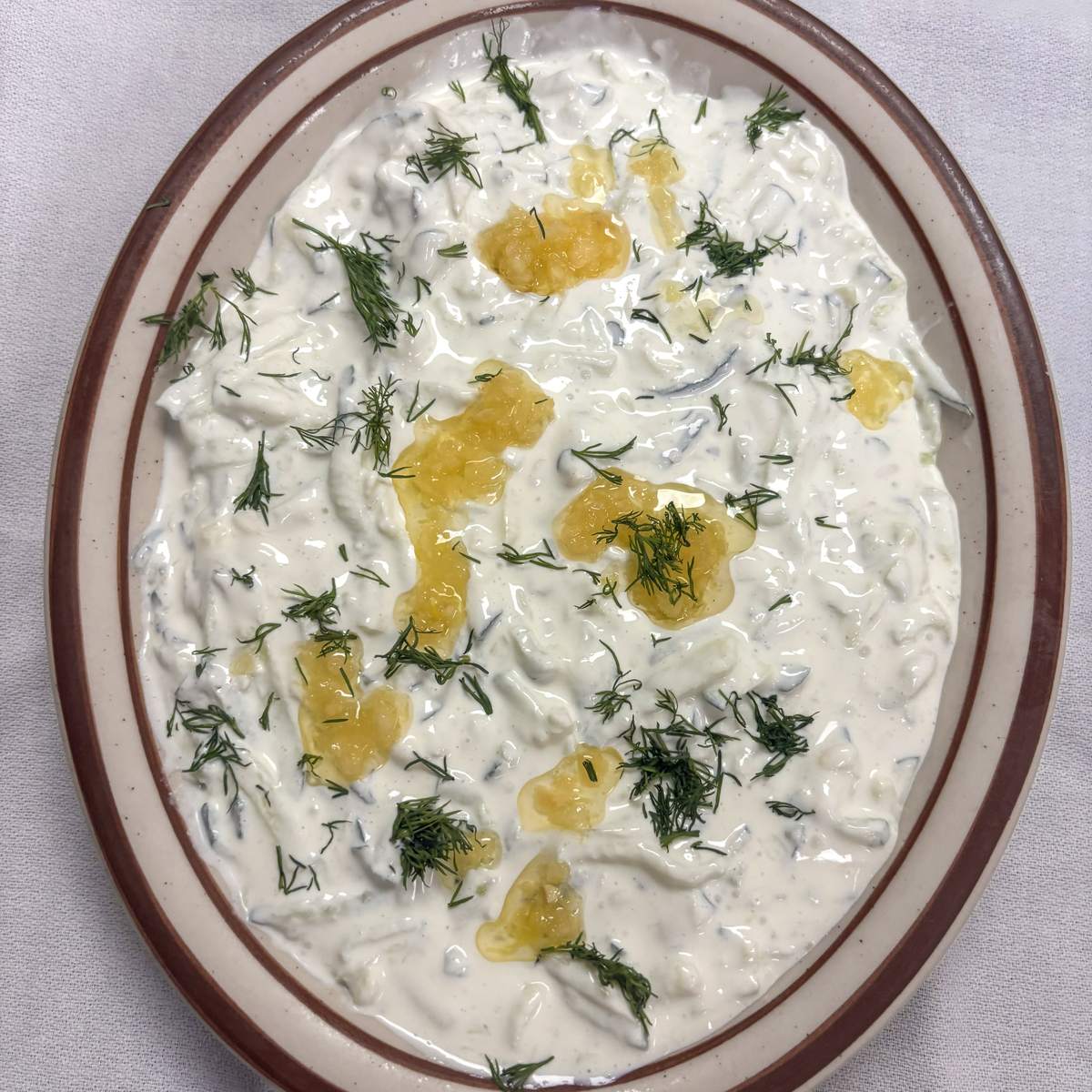 A bowl of housemade tzatziki drizzled with olive oil and topped with fresh dill.