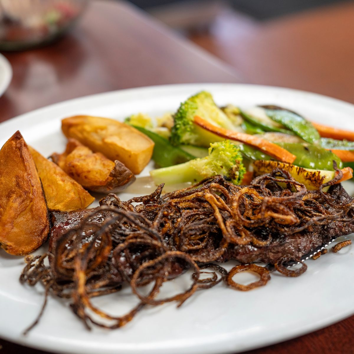 Skirt steak topped with crispy fried onions, served with steak fried potatoes and grilled vegetables.